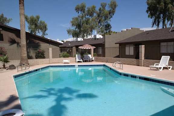 A swimming pool in a backyard with a patio and trees.