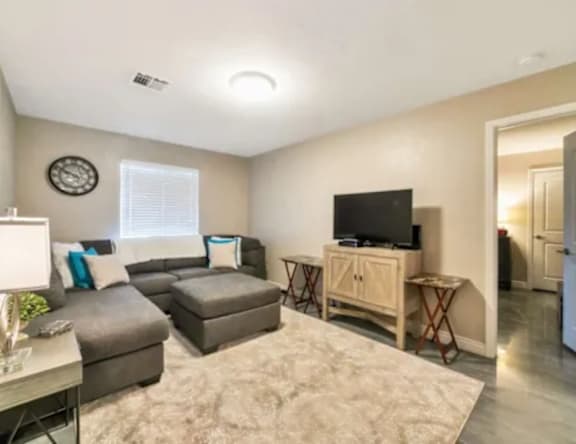 A living room with a grey couch, a white table, and a flat screen TV.