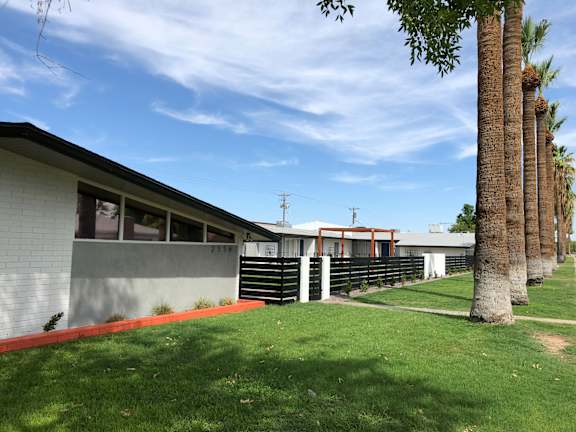 A white building with a red stripe on the side is surrounded by palm trees.