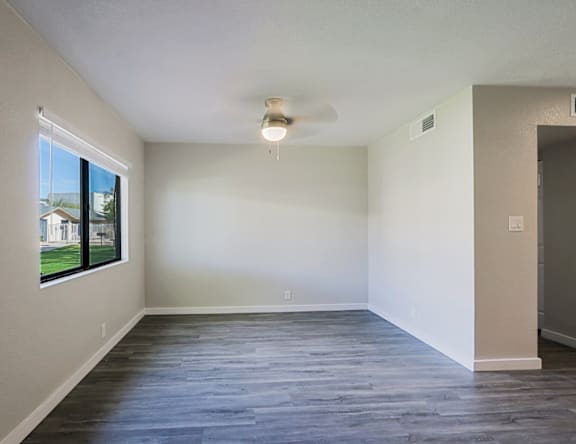 A spacious room with a ceiling fan and a window overlooking a lawn.