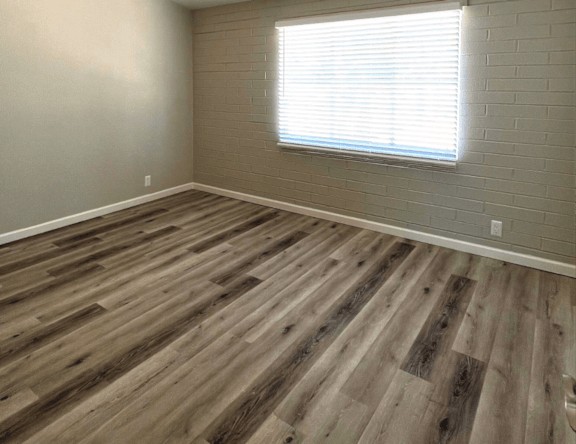 A room with wooden flooring and a window with blinds.