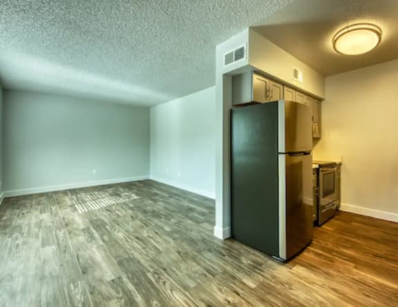 A kitchen area with a black fridge and wooden flooring.