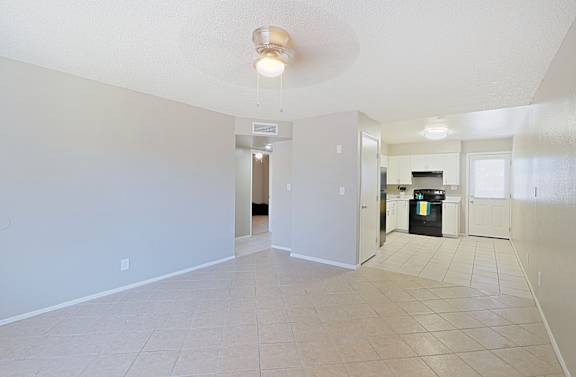 A spacious, empty room with a kitchen area in the background.