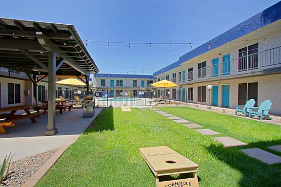 A cornhole board sits in the grass of a courtyard.