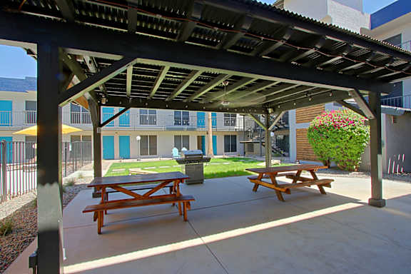 A wooden picnic table is under a roof on a patio.