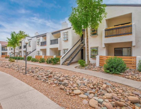 A row of white buildings with balconies and a gravel path in front.