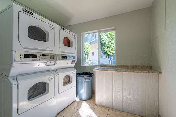 A laundry room with a stack of washing machines and a window.