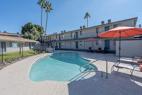 A pool surrounded by a concrete patio and a red umbrella.