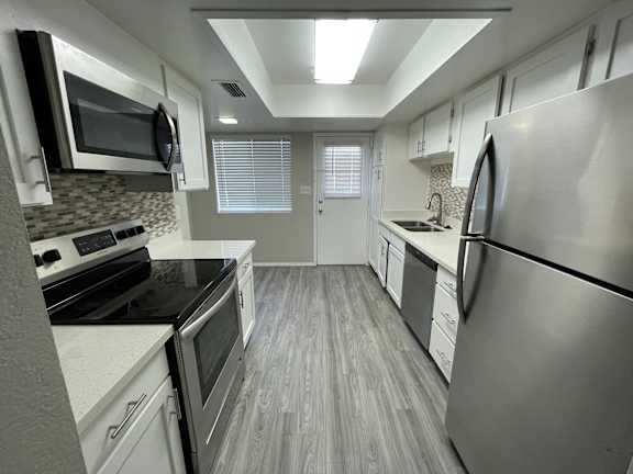 A modern kitchen with stainless steel appliances and wooden flooring.