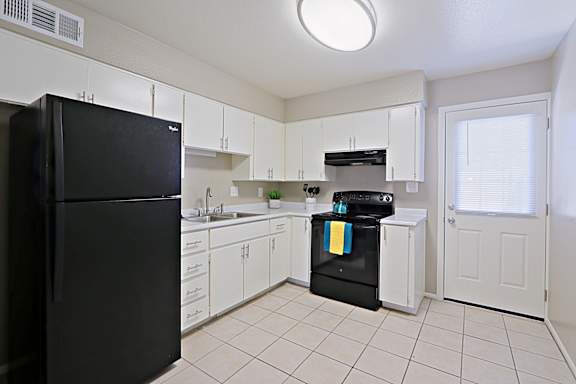A black refrigerator stands in a kitchen with white cabinets and a black dishwasher.