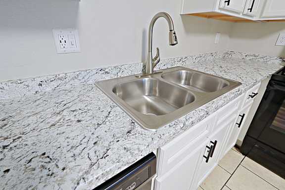 A kitchen with a granite countertop and a stainless steel sink.