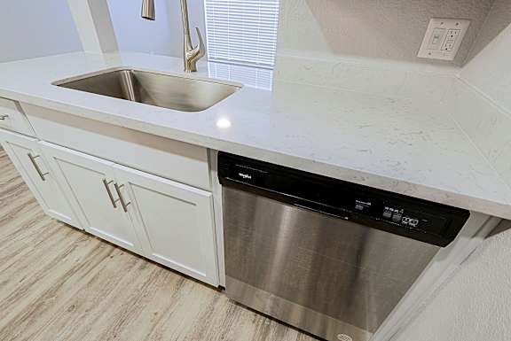 A modern kitchen with a stainless steel dishwasher and white cabinets.