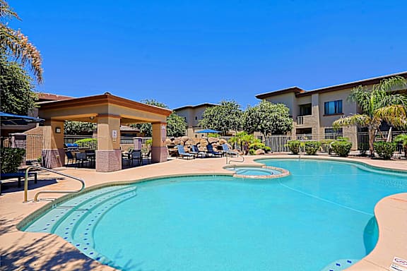 A large swimming pool in front of a building with people sitting on chairs.