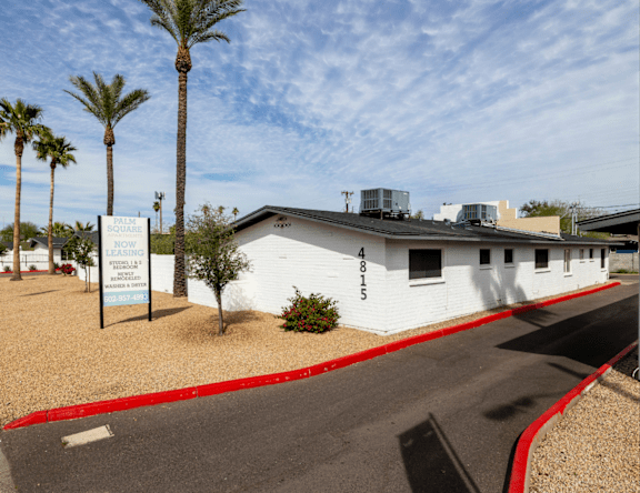 A white building with a sign that says "Square One Apartments" in front of it.