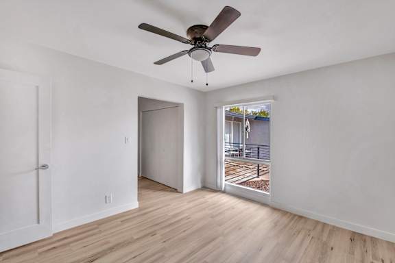 A room with a ceiling fan and a view of a train track outside the window.