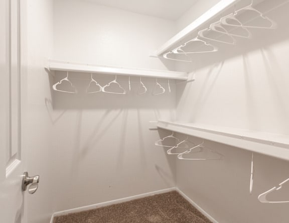 A white closet with hangers on the shelves.