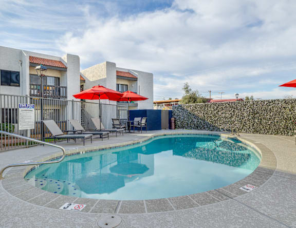 A round swimming pool with a blue tinted water and a red umbrella.