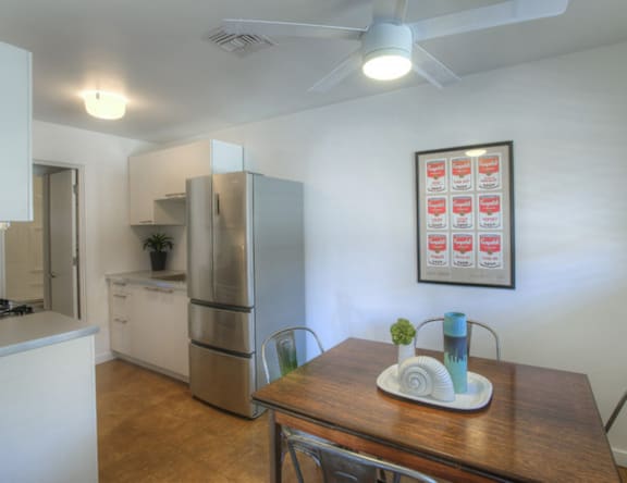 A kitchen with a refrigerator, a table with a tray on it, and a ceiling fan.
