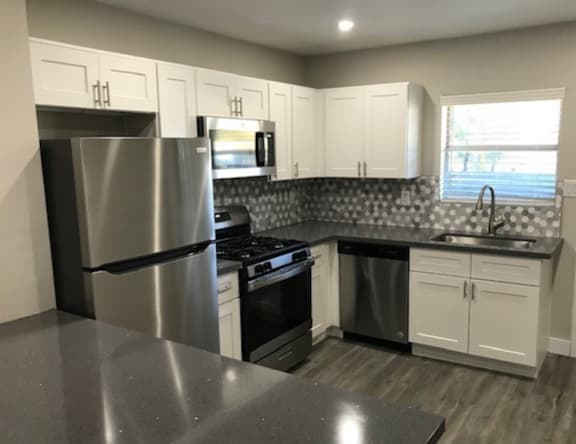 A kitchen with a stainless steel refrigerator, black countertops, and white cabinets.