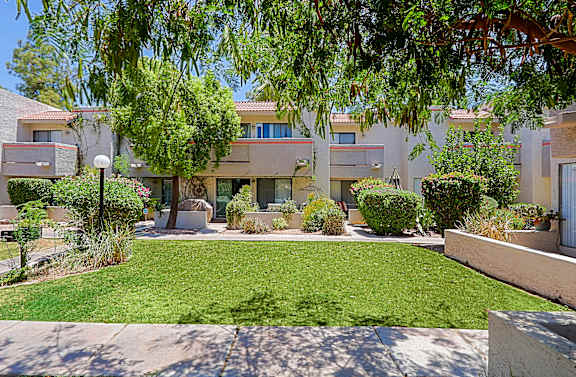 A sunny day at a residential complex with a well-maintained lawn and trees.