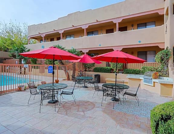 A patio with red umbrellas and a pool in the background.