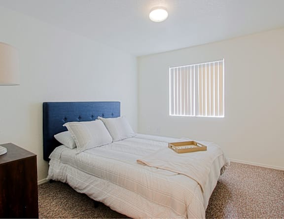 A bed with a blue headboard and white bedding sits in a room with a carpeted floor.