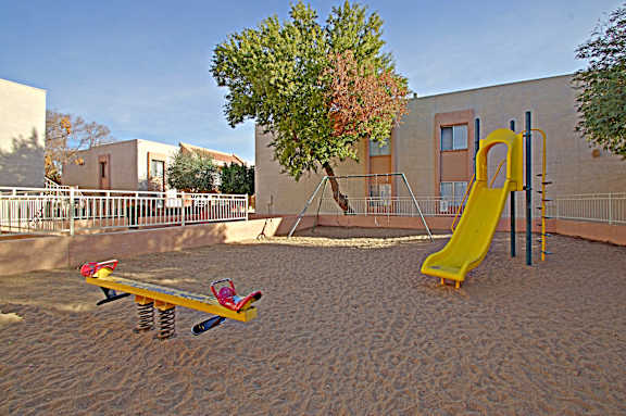 A playground with a yellow slide and a red and yellow seesaw.