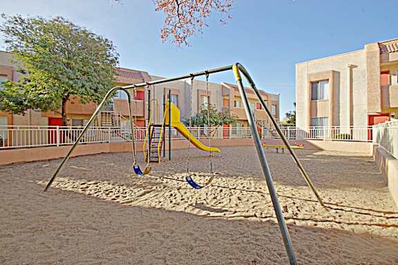 A playground with a yellow swing set in the middle of a sandy area.