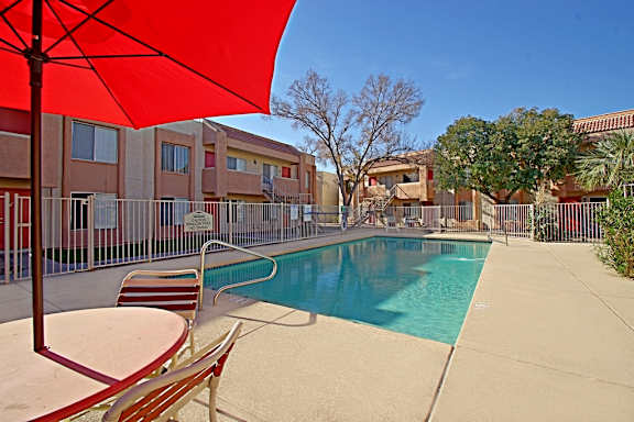 A red umbrella is next to a swimming pool.