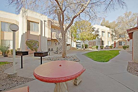 A red table is in the middle of a courtyard with a tree and apartment buildings in the background.