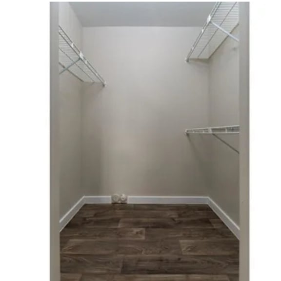 A room with white walls and wood flooring with two shelves on the wall.