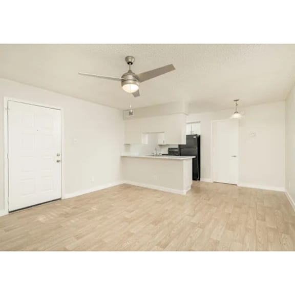 A room with a ceiling fan and light, a door, and a kitchenette with a black fridge and microwave.