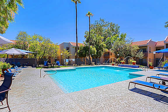 A swimming pool surrounded by chairs and trees.