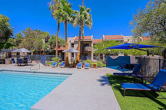 A pool surrounded by palm trees and lounge chairs.