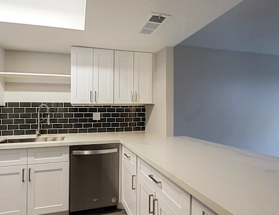 A kitchen with white cabinets and a black tile backsplash.