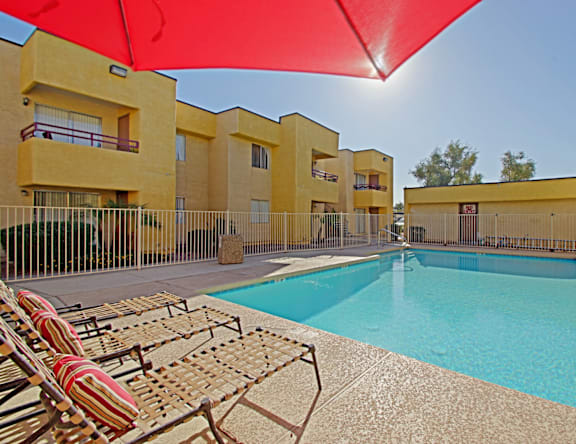 A pool area with sun loungers and a red umbrella.