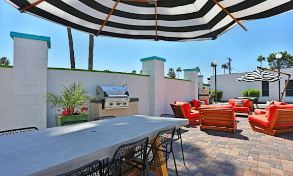 A patio with a table, chairs and a grill under a striped umbrella at Palm Villas Apartments, Scottsdale, AZ