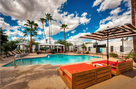 A pool area with sun loungers and palm trees at Palm Villas Apartments, Scottsdale Arizona