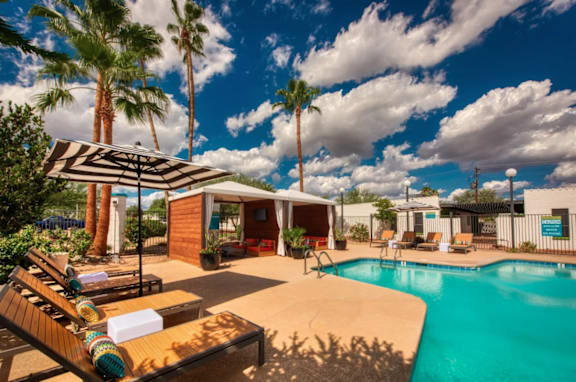 A poolside area with a sun lounger and a striped umbrella at Palm Villas Apartments, Arizona