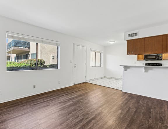 A spacious room with wooden flooring and a window overlooking a building.