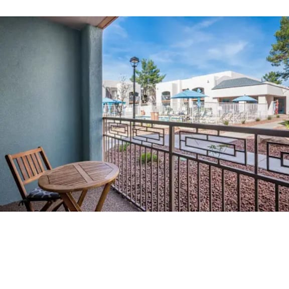 A wooden chair sits on a patio with a table and a metal railing.