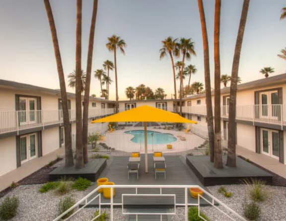 A pool surrounded by palm trees and a yellow umbrella.