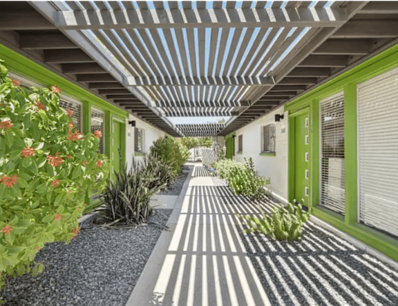 A long hallway with green doors and plants on the sides.