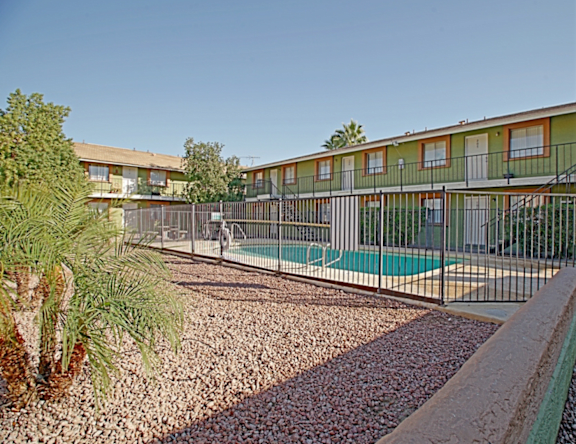 A pool surrounded by a metal fence and a gravel area in front of a building.