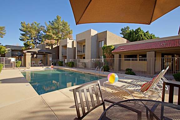 A pool with a chair and umbrella in front of a building.