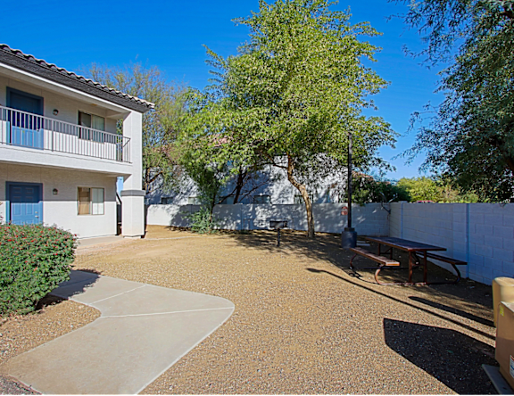 A white building with a balcony is surrounded by a gravel courtyard.