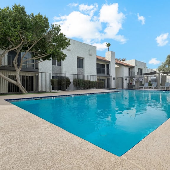 A swimming pool in front of a white building with a tree on the left.