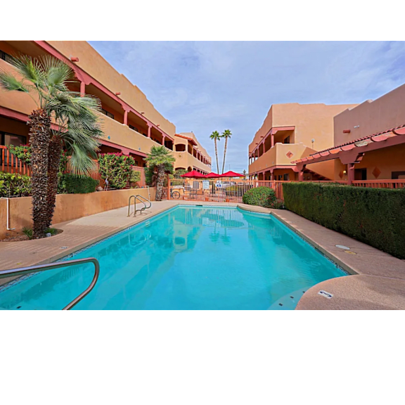 A swimming pool in front of a building with palm trees.