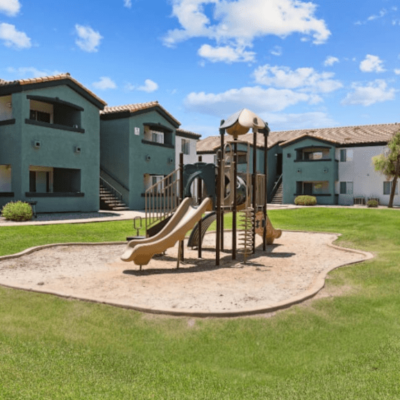 A playground with a yellow slide in front of a building.
