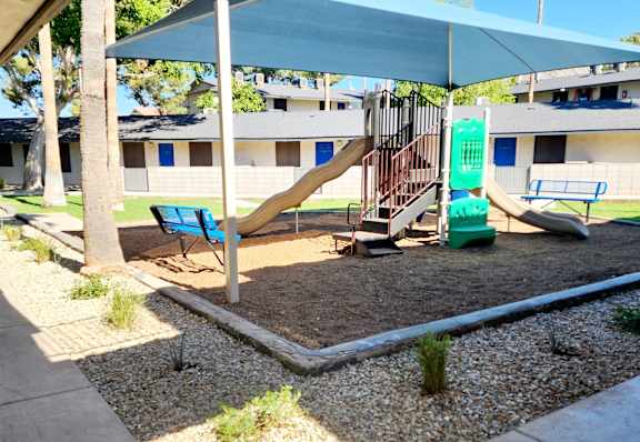 A playground with a slide, swings, and a bench under a blue canopy.